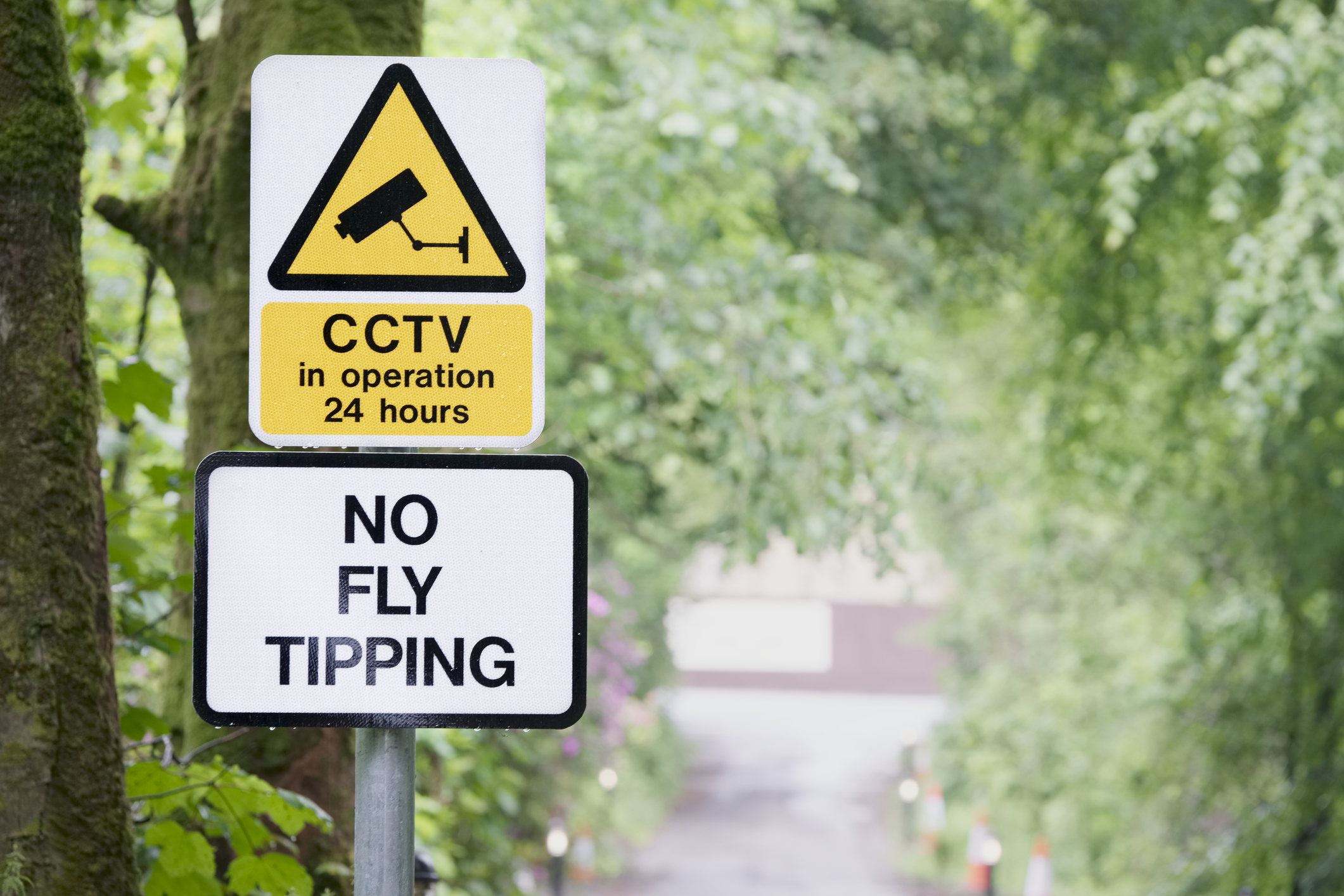 No fly tipping sign with CCTV sign against background of tree lined country road