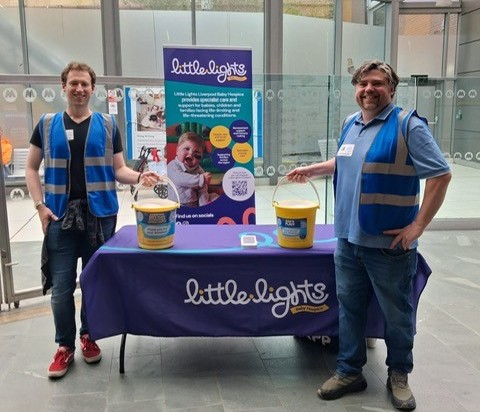 2 people standing either side of a table with charity collection buckets