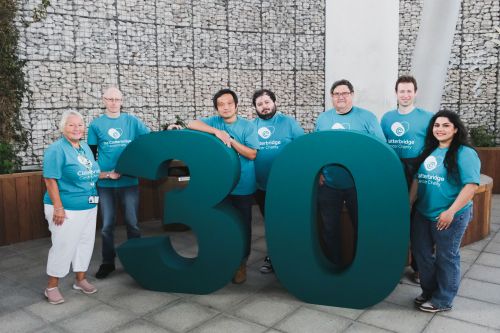 seven people in teal t-shirts standing behind number 30